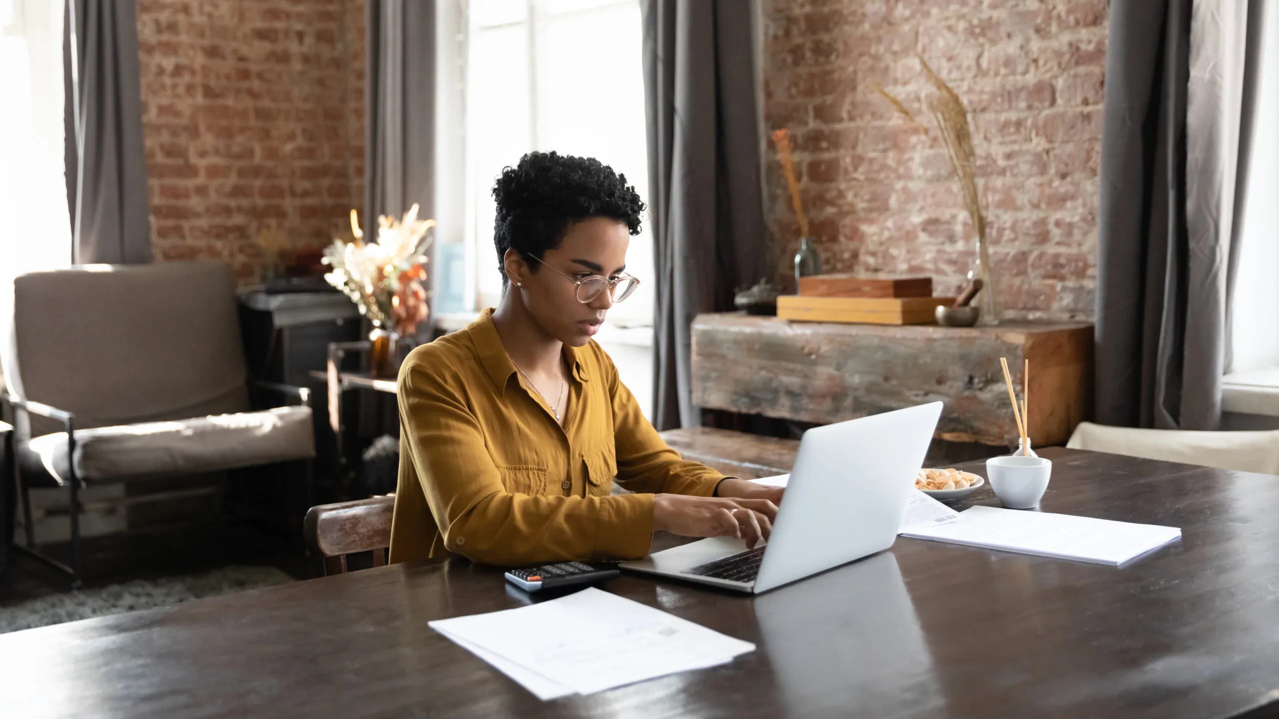 Young woman working on a laptop surrounded by paperwork contemplating how long does it take to get approved for an apartment.