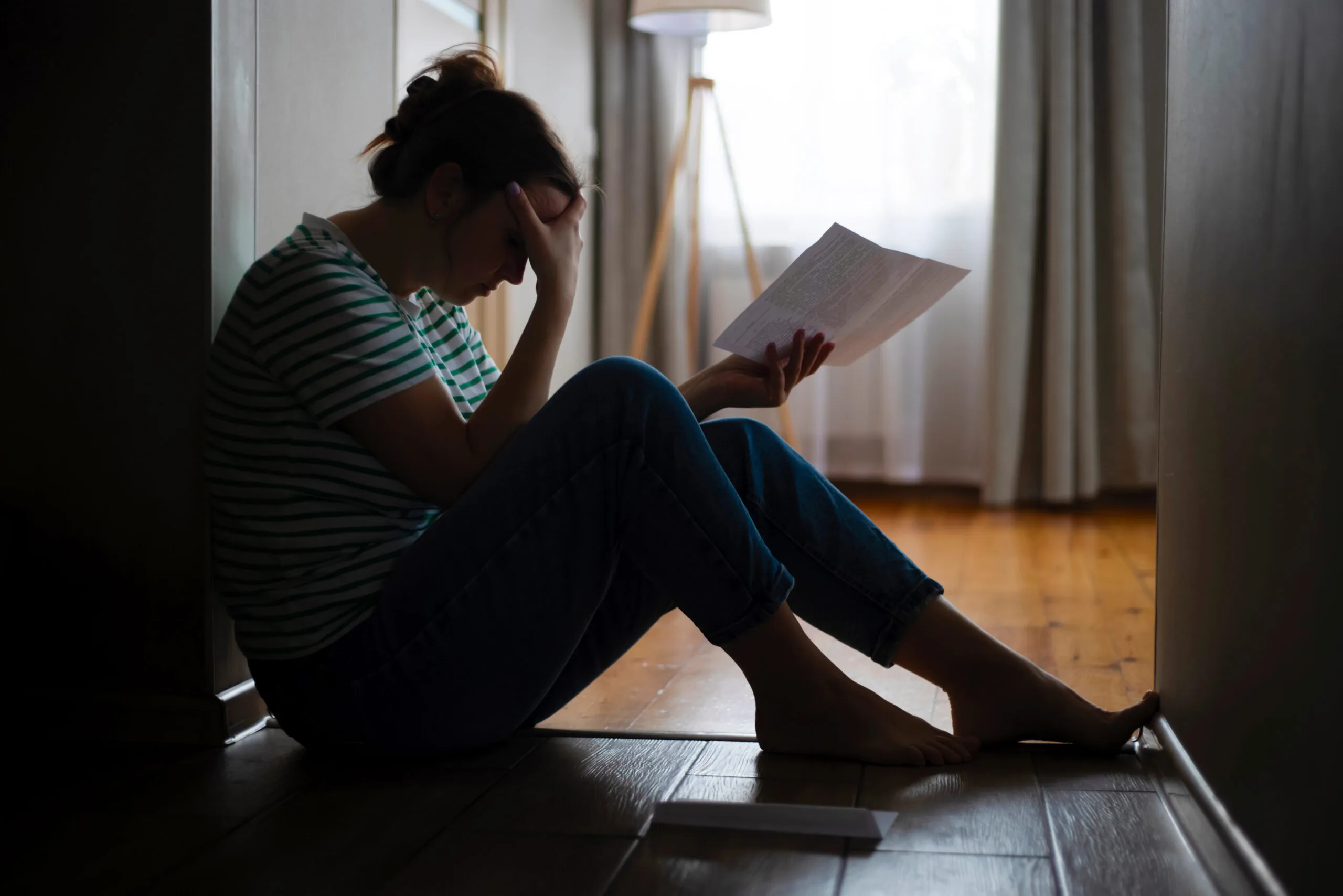 Silhouette of a sad woman sitting on the floor of her apartment. Getting bad news, eviction, depression, trouble.