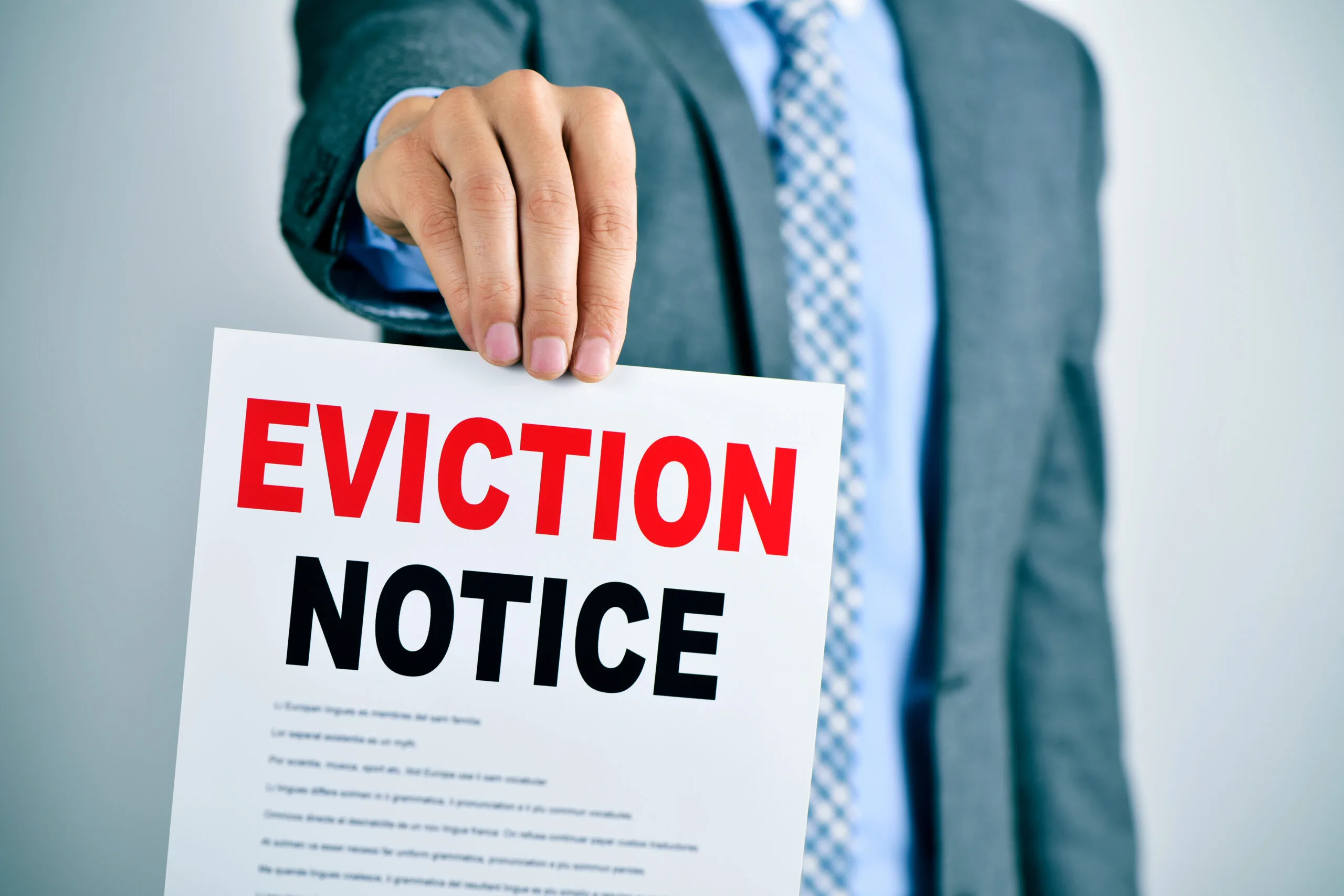 A young caucasian man wearing a gray suit shows a document with the text eviction notice.
