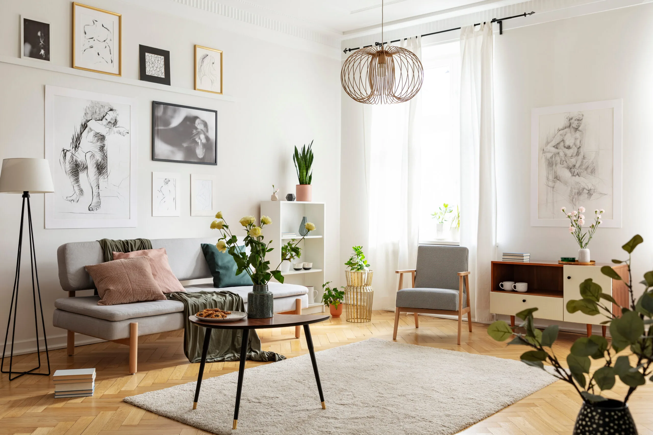 Table with flowers on carpet in apartment interior with posters above sofa near armchair