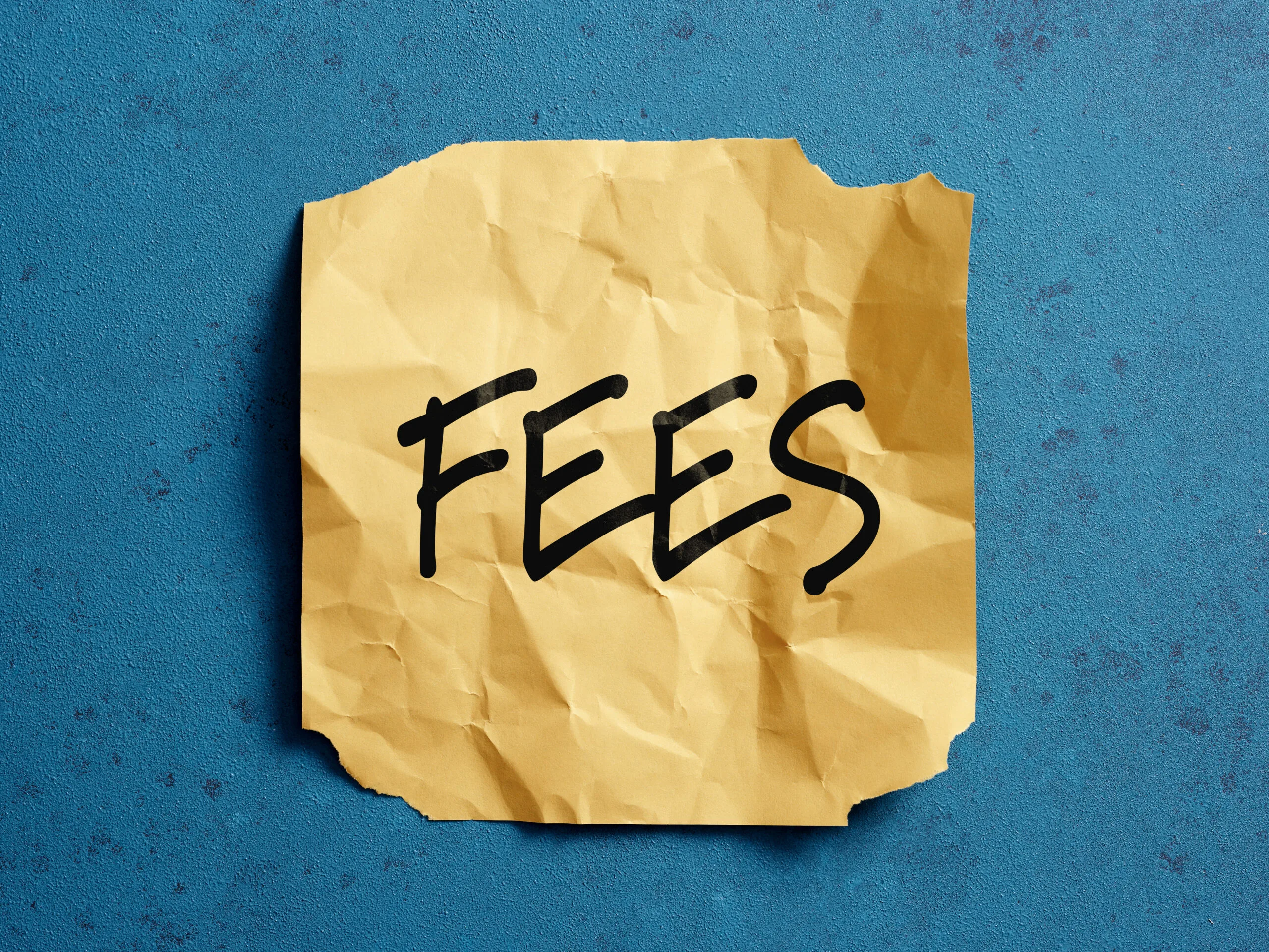 Fees written on crumpled yellow paper note on blue background representing business, financial and tax concepts