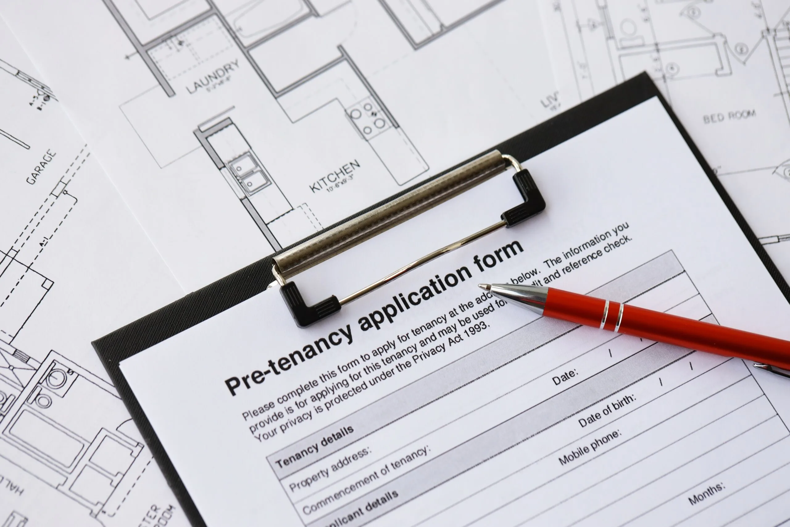 Pen on pre-tenancy application form and planning blueprints of residential building project close up.