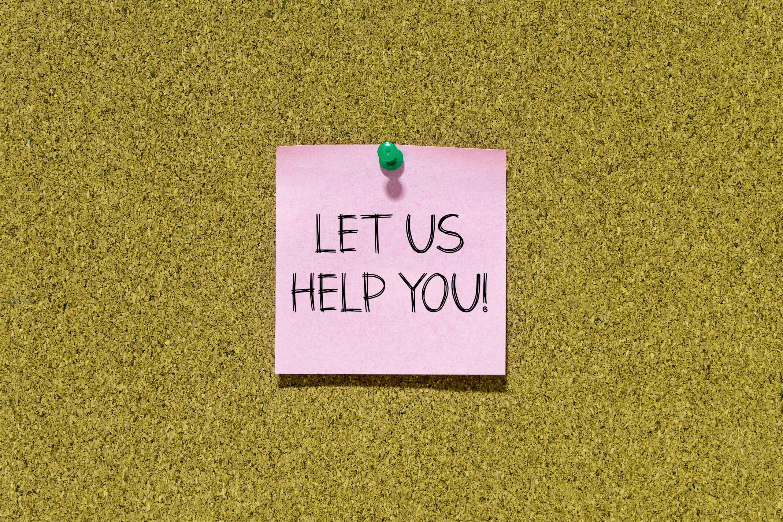 Let us help you text on pink post-it paper pinned on bulletin cork board. 