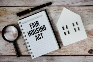 Fair Housing Act text on paper notebook with white house model and magnifying glass on wood background