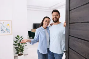 Happy couple welcoming near door. Invitation to come indoors