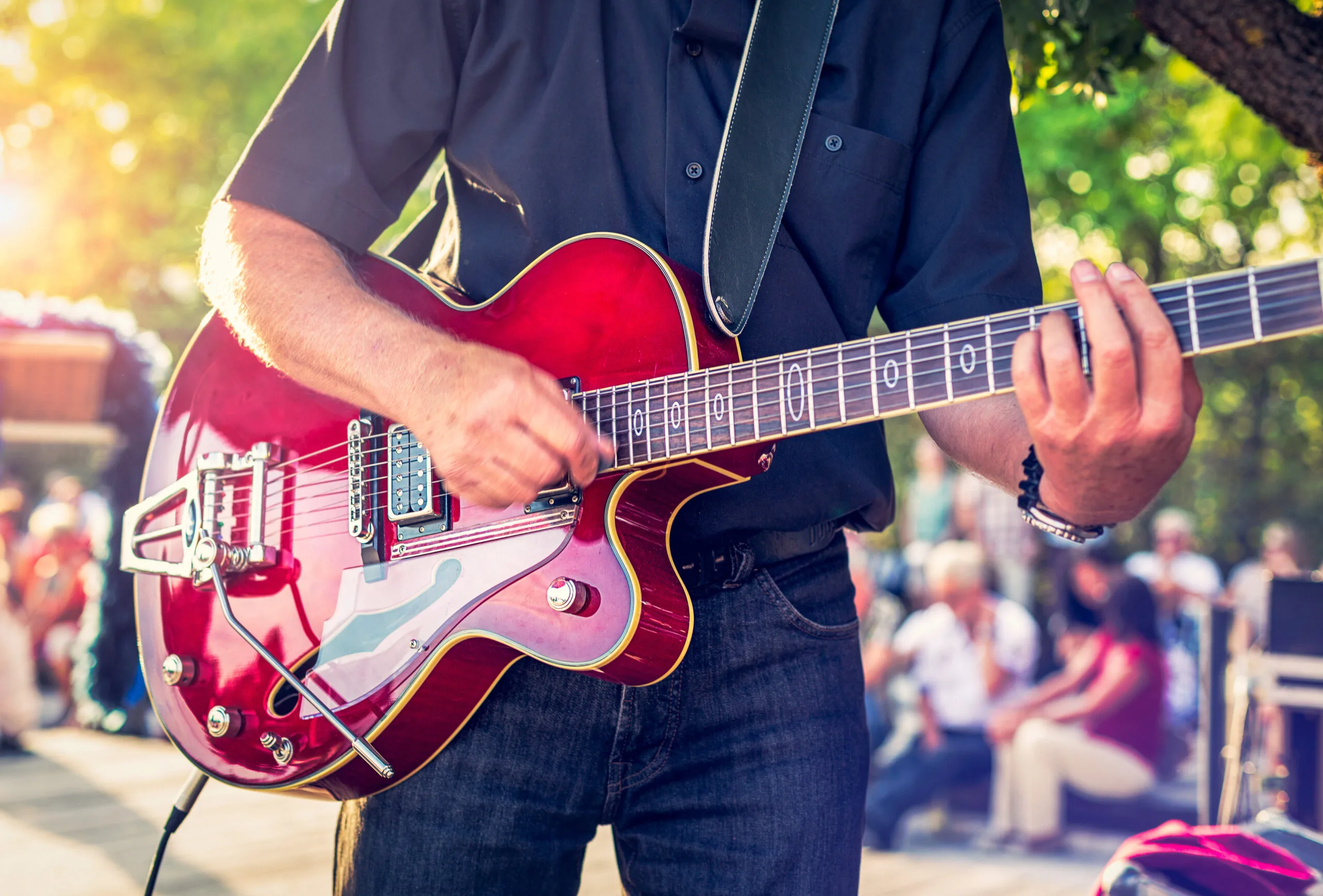 Man with a red electric guitar in the park playing a summer concert | Bay Management Group Texas